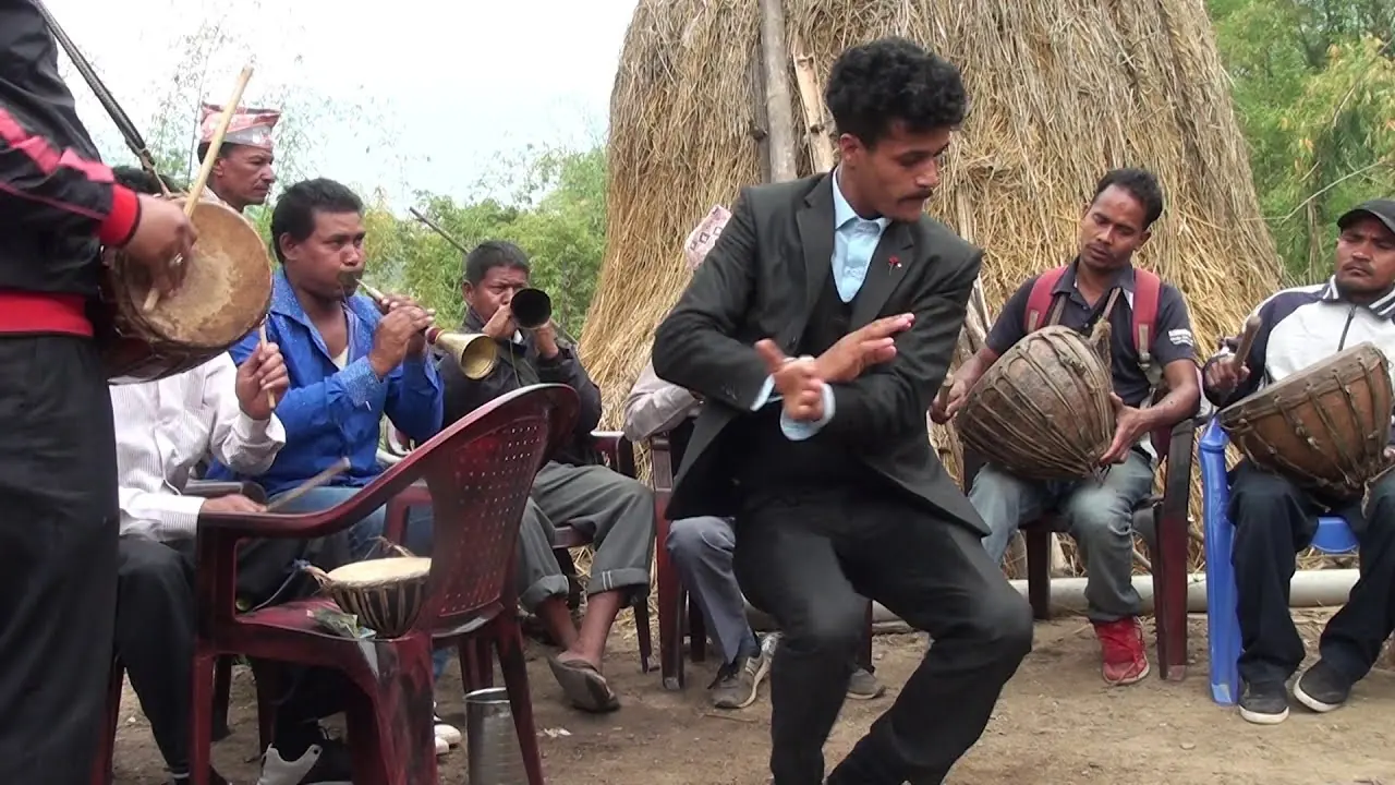 A panchebaja band plays drums and horns outdoors in Arjunchaupari while a man in a suit dances in front of them