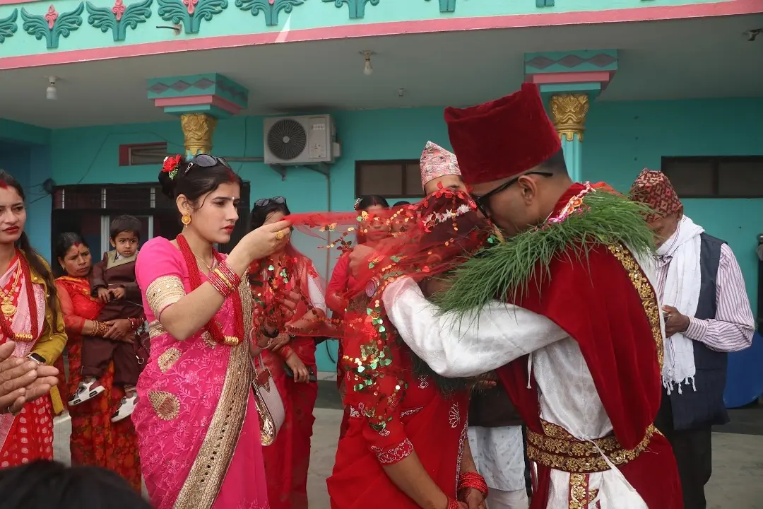 Relatives in red and pink welcome the groom in his dhaka topi and garland at the bride's home in Syangja